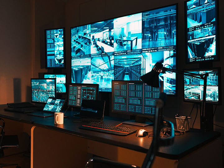 Business security command center showing security camera feeds and laptops with controls on the desk