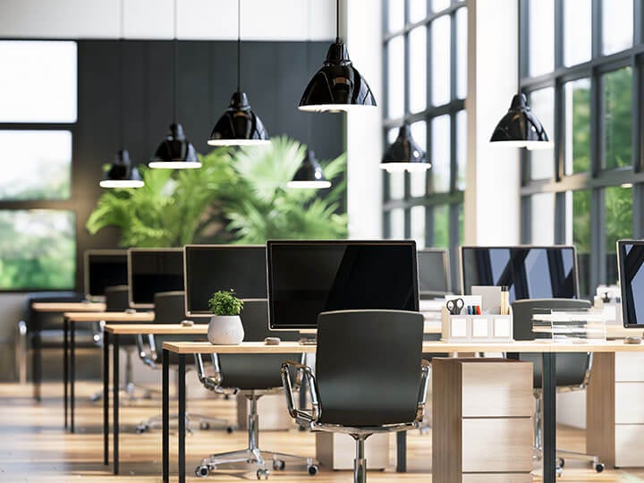 Modern loft style office with black computers, chairs, and lights, decorated with green nature