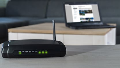 A wireless router placed on a table beside a laptop, showcasing a modern home office setup.